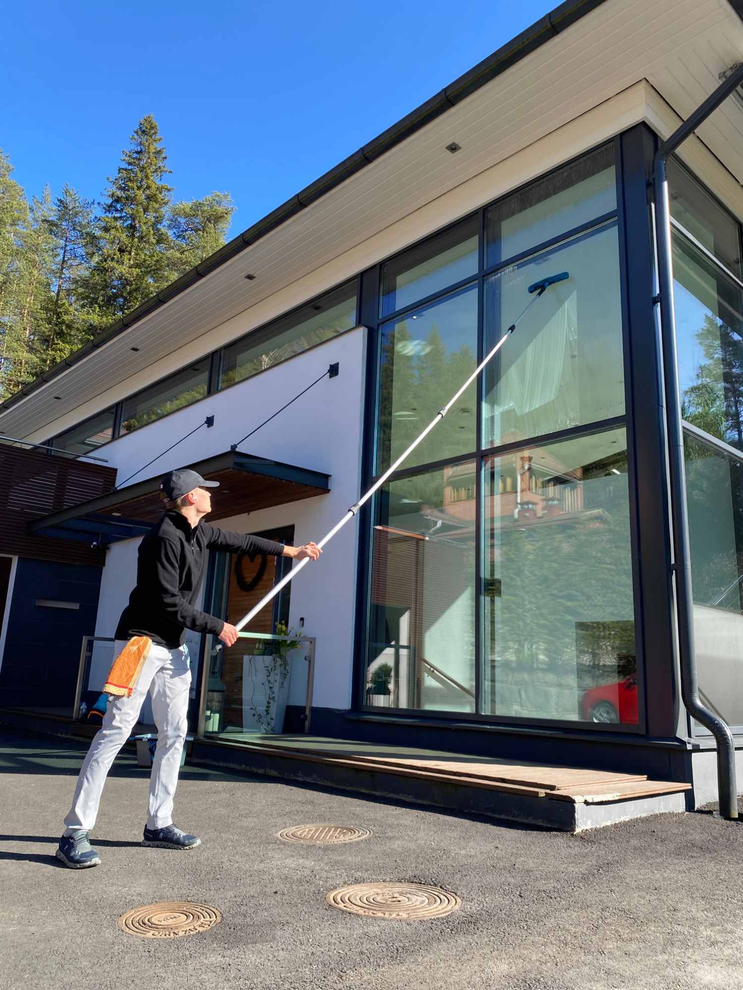 PB & Co:n perustaja pesee modernin talon korkeaa lasiseinää jatkovarrella aurinkoisena kevätpäivänä.