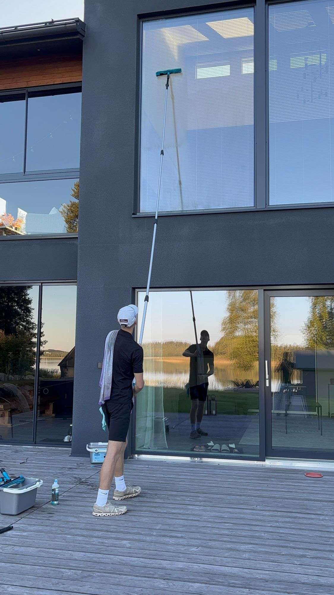 Perustaja pesee kaksikerroksisen talon lasiseinää jatkovarrella.
